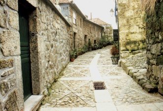 [Rua dos Moreirais, Bairro do Castelo: calcetada, estreita e em declive, ladeada por casas baixas de paredes de pedra]