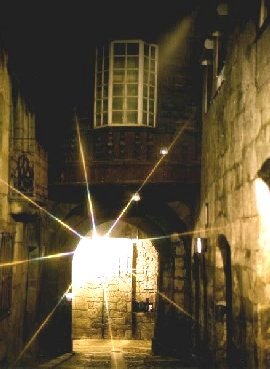 [Porta da Vila: À noite, uma luz brilhante atrás do arco a realçar o ambiente misterioso e romântico do castelo]